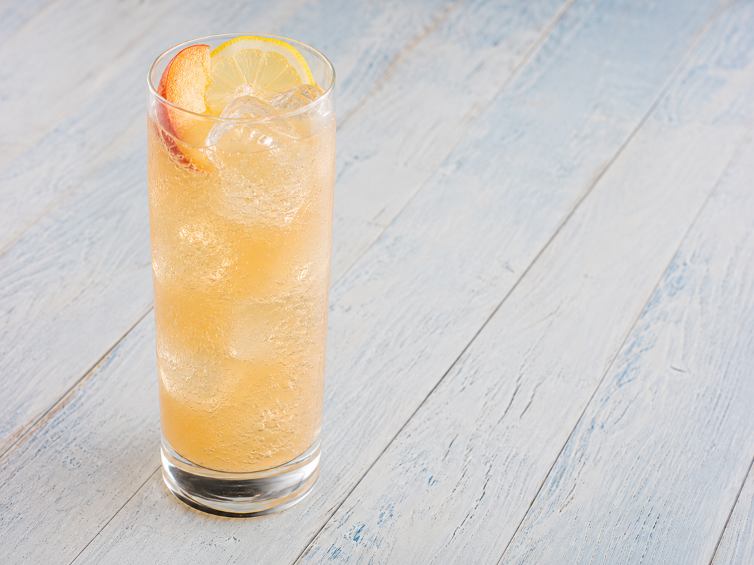 White Tea Peach Fizz in a tall glass with ice, peach slice, and lemon wheel